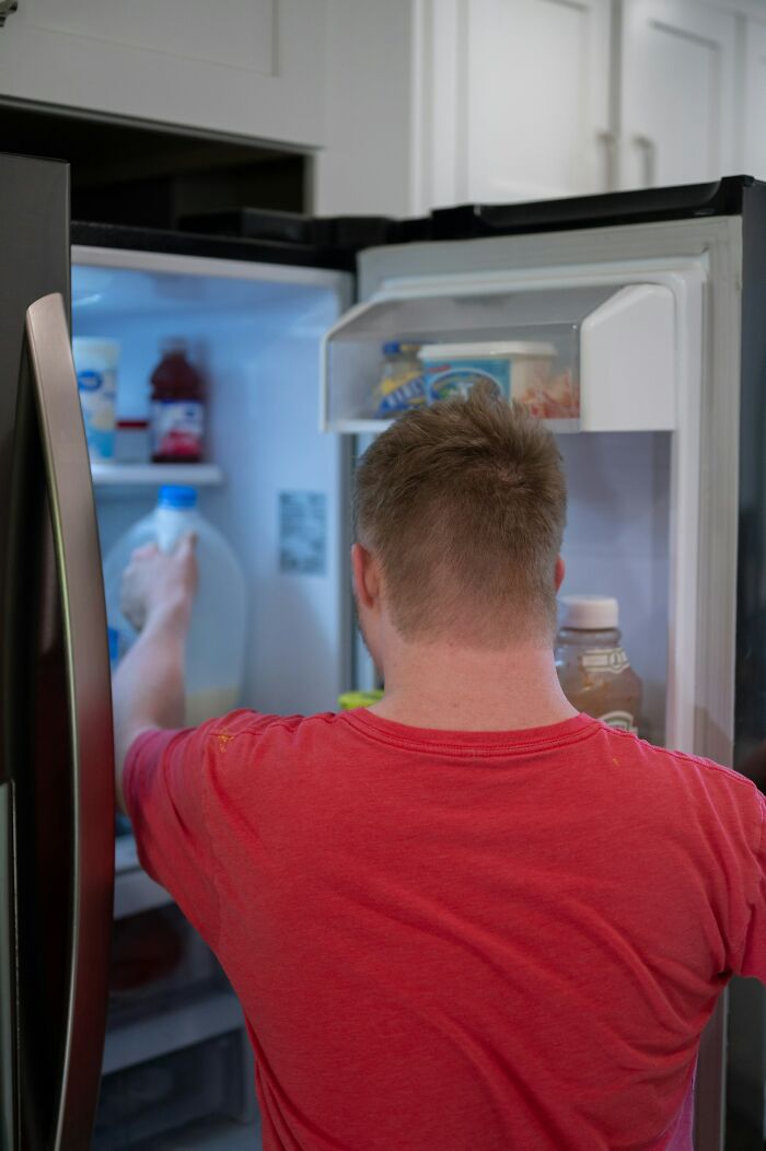 Hombre abriendo el refrigerador buscando comida, capturando un momento cotidiano relacionado con karma real y reacciones sinceras.