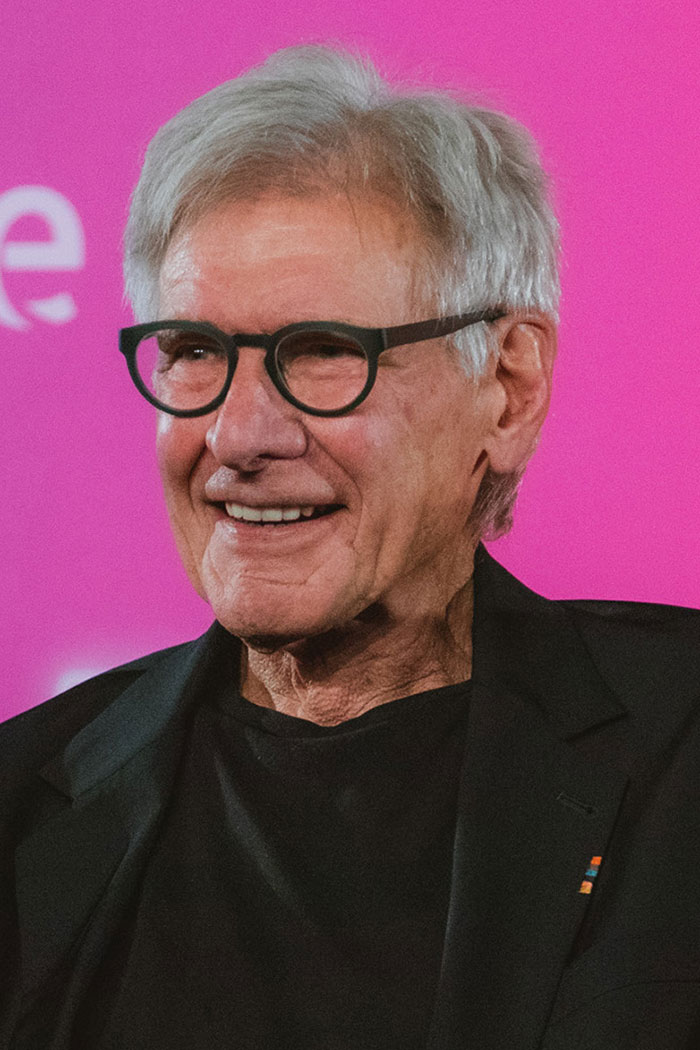 Hombre mayor con gafas negras sonriendo en evento con fondo rosa, relacionado con celebridades y basketball en silla de ruedas. Hombre mayor con gafas negras sonriendo en evento con fondo rosa, relacionado con celebridades y basketball en silla de ruedas.