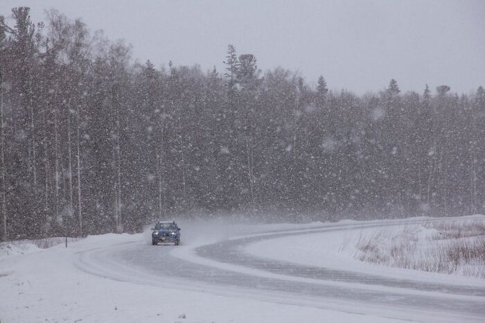 Coche conduciendo por carretera nevada en bosque durante tormenta de nieve, reflejando momentos de karma instantáneo. Coche conduciendo por carretera nevada en bosque durante tormenta de nieve, reflejando momentos de karma instantáneo.