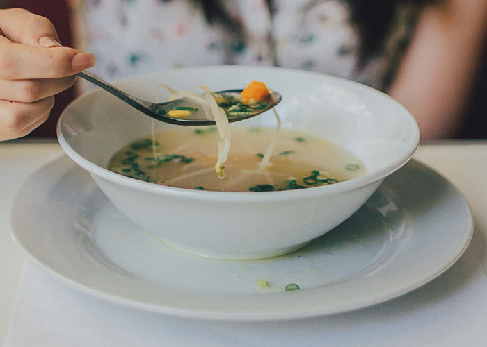 Persona sosteniendo cuchara con sopa clara y vegetales, relacionada con hallazgos sorprendentes en autopsias médicas. Persona sosteniendo cuchara con sopa clara y vegetales, relacionada con hallazgos sorprendentes en autopsias médicas.