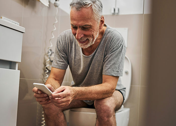 Hombre mayor sentado en el baño usando teléfono móvil, relacionado con hallazgos sorprendentes de médicos forenses. Hombre mayor sentado en el baño usando teléfono móvil, relacionado con hallazgos sorprendentes de médicos forenses.