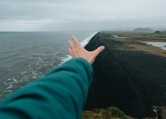Brazo extendido hacia el océano con una playa negra al fondo, representando momentos de karma instantáneo.