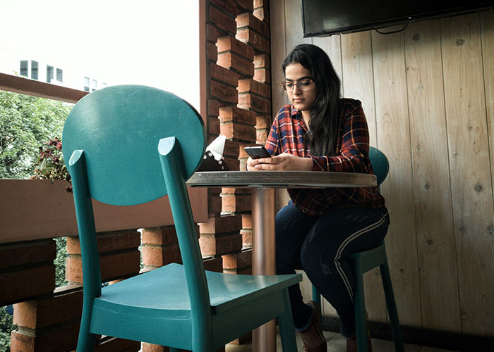 Mujer sentada en cafetería usando el móvil, ilustrando momentos de karma instantáneo y consecuencias merecidas.