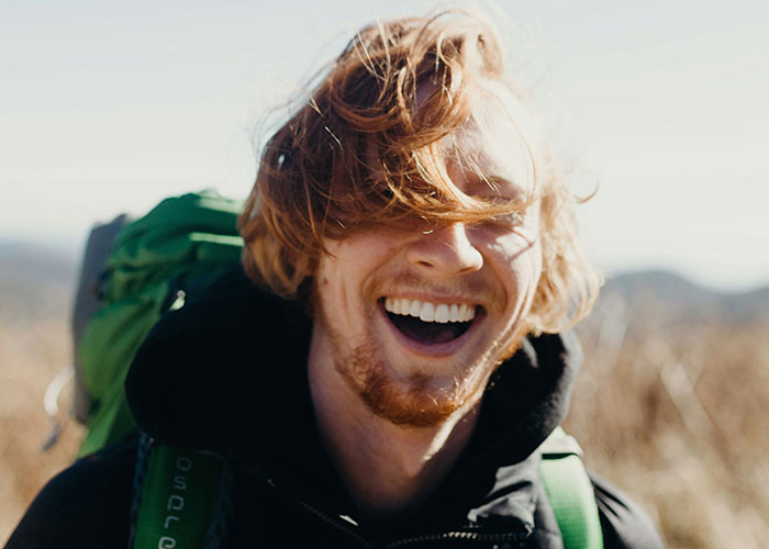 Joven con mochila verde sonriendo al aire libre, ilustrando momentos de karma instantáneo y justicia en la vida.