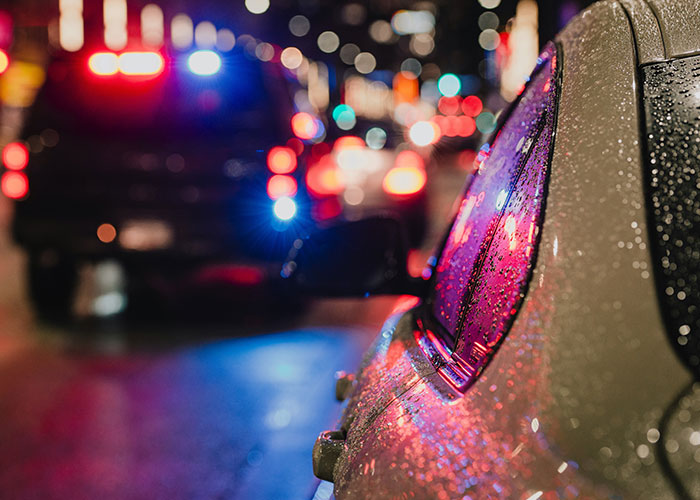 Coche detenido bajo la lluvia con luces policiales al fondo, simbolizando momentos de karma instantáneo y justicia.
