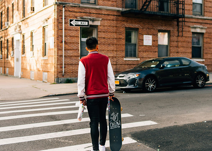 Joven con patineta cruzando calle al lado de un carro, simbolizando momentos de karma instantáneo recibido.