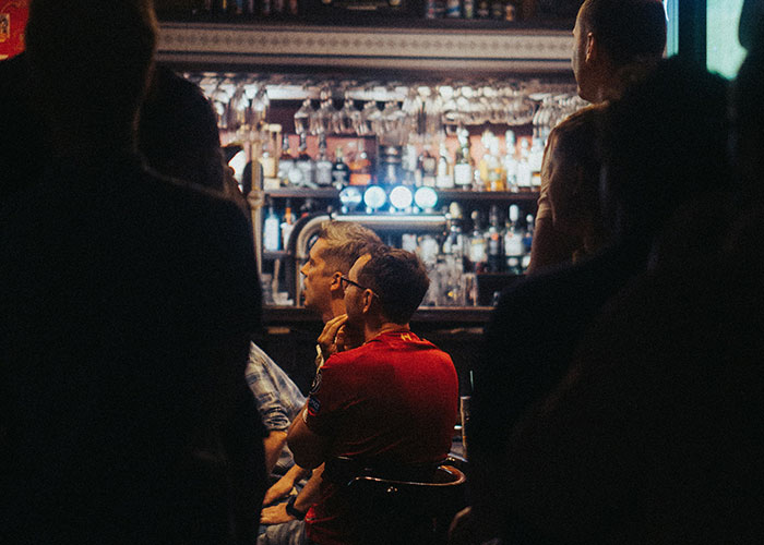 Personas en un bar observando un momento de karma instantáneo mientras se desarrolla la acción en un ambiente oscuro.
