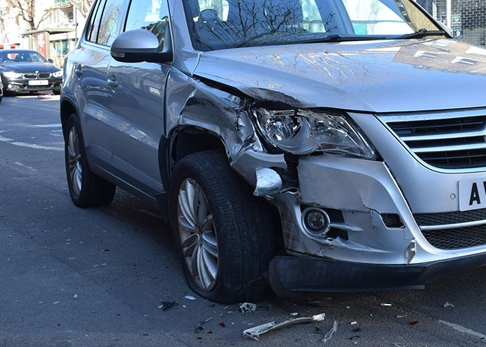 Auto gris con daño severo en la parte delantera izquierda tras un choque, ejemplo de momentos de karma instantáneo.