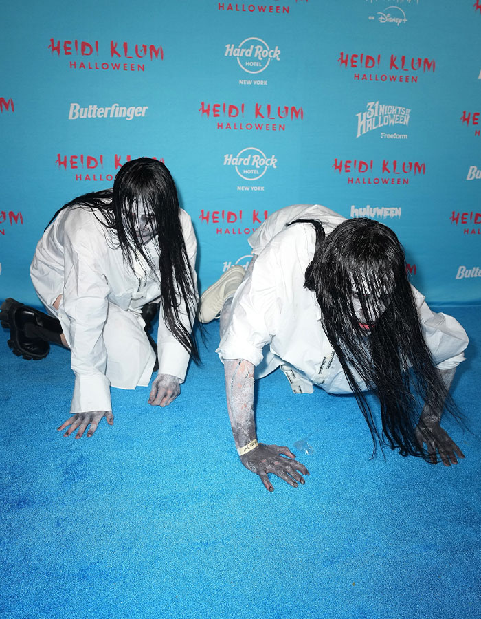 Dos personas con disfraces de celebridades de Halloween, maquillaje blanco y cabello largo en evento Heidi Klum 2025.