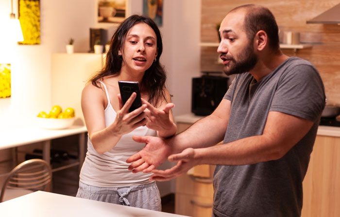 Pareja discutiendo en la cocina mientras ella muestra algo en su teléfono, representando historias de drama familiar caótico.