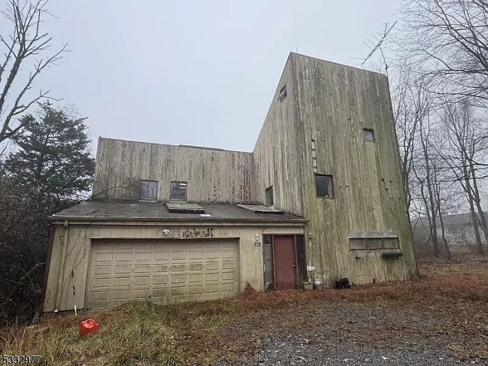 Casa en listado de Zillow en mal estado con fachada desgastada, ventanas pequeñas y entorno descuidado en un día nublado.