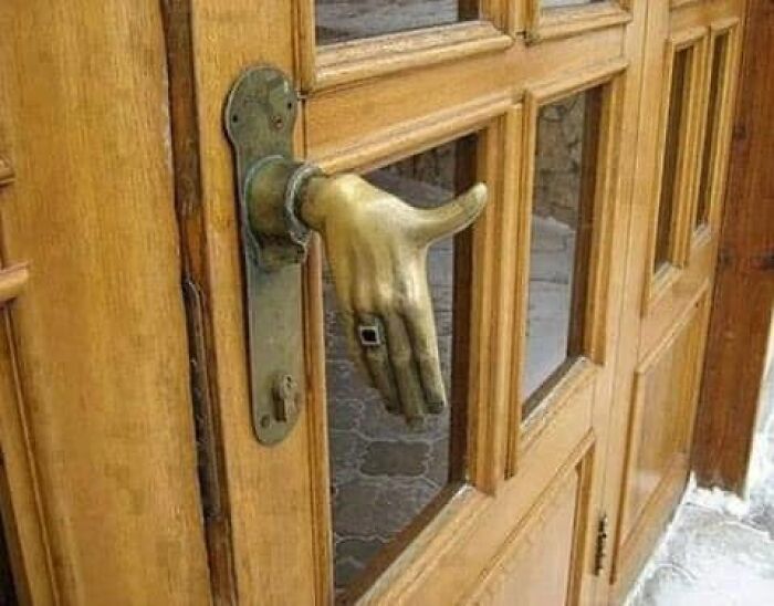 Manija de puerta con forma de mano de bronce en una puerta de madera, ejemplo de listados Zillow tan malos que parecen falsos.