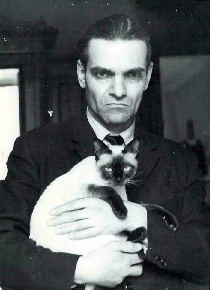 Hombre serio de época con gato siamés en foto rara y poderosa de comunidad histórica online.