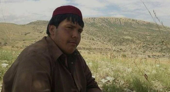 Hombre con gorro rojo sentado en campo abierto, parte de fotos raras y poderosas de comunidad histórica en línea.