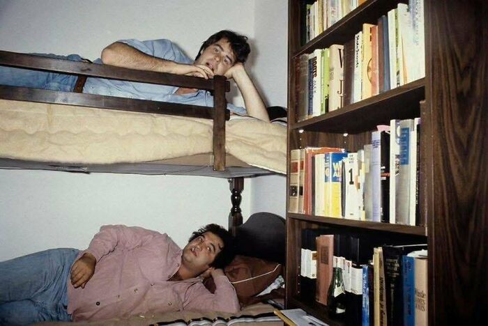 Dos hombres descansan en literas junto a una estantería llena de libros en una foto rara y poderosa de historia.