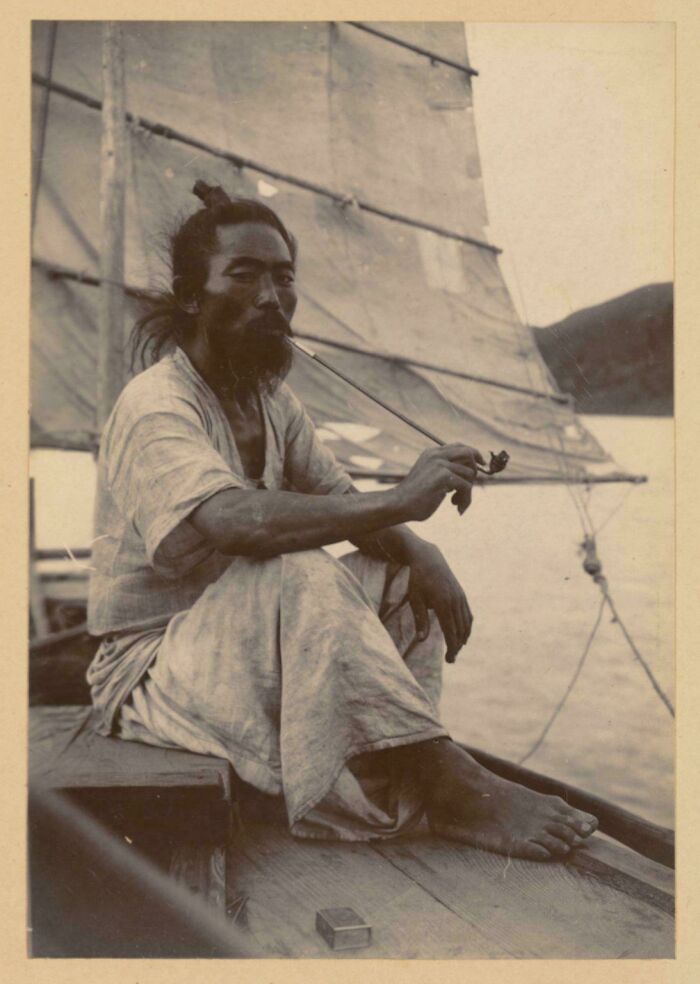 Hombre histórico fumando en barco tradicional, foto rara y poderosa de comunidad en línea enfocada en historia.