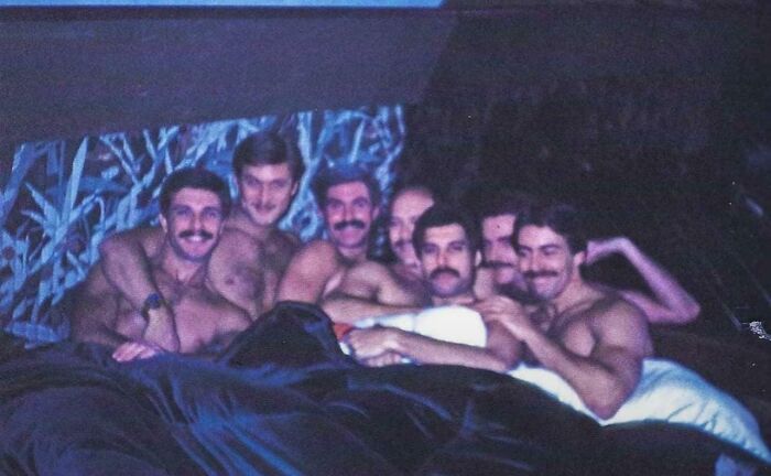 Grupo de hombres con bigote en cama, foto única y poderosa de comunidad en línea enfocada en historia.