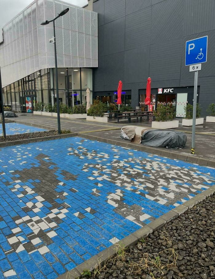 Plaza de estacionamiento para discapacitados con mosaicos azules desgastados mostrando fallos divertidos por seguir instrucciones demasiado estrictas.