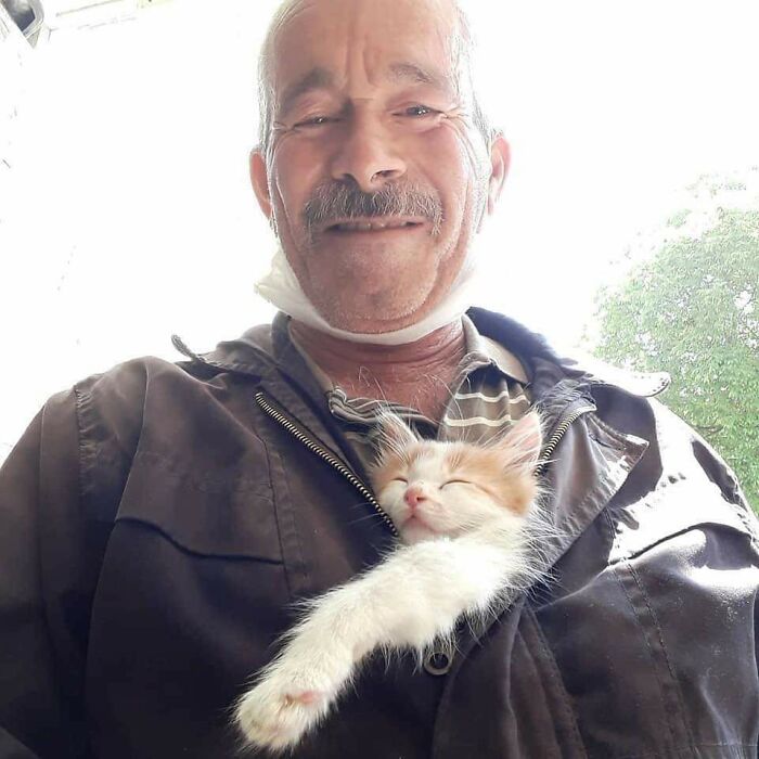 Hombre sonriente con gato durmiendo en su chaqueta en una tierna selfie de animales divertida y conmovedora.