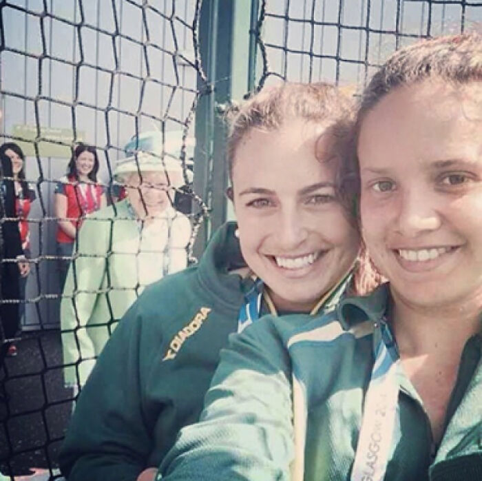 Dos mujeres sonrientes en selfie con cameo inesperado de una persona vestida de verde, arruinando la foto divertida.