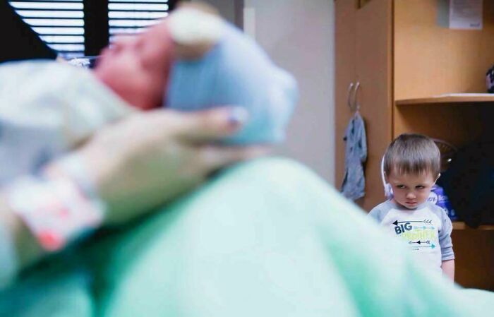 Niño con expresión divertida arruinando foto de recién nacido en hospital, ejemplo claro de fotos arruinadas por cameos inesperados.