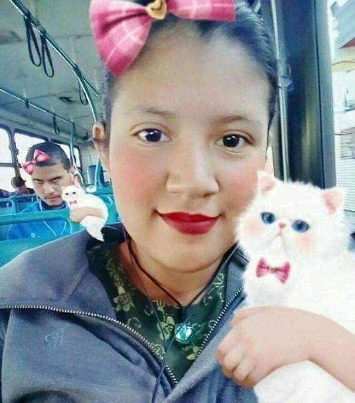 Mujer con gato blanco y lazos rosas en selfie en autobús con cameo inesperado y expresión divertida de hombre detrás.