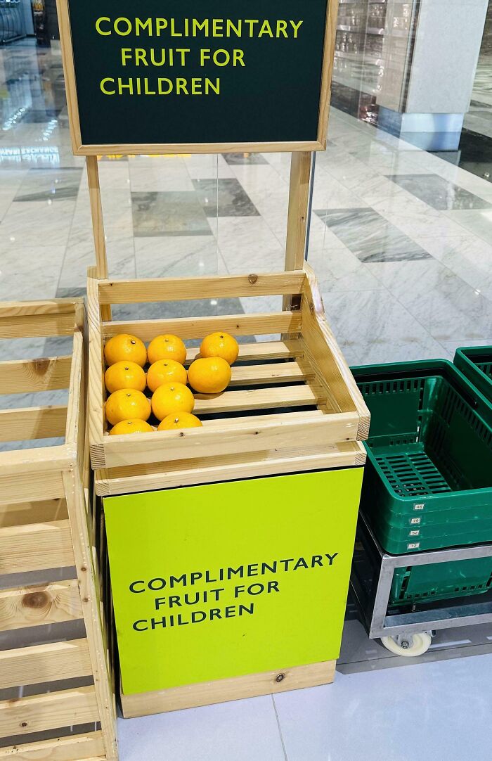Frutas gratis para niños en caja de madera, solución inteligente para problemas cotidianos en un espacio público moderno.
