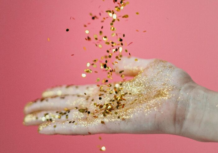 Mano con brillantina dorada cayendo sobre fondo rosa, simbolizando acciones de venganza contra ex parejas.