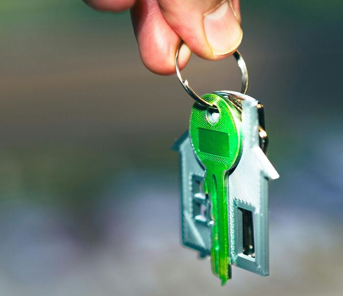 Llave verde con llavero en forma de casa sostenida en mano, simbolizando venganza y cierre de relaciones con ex parejas.