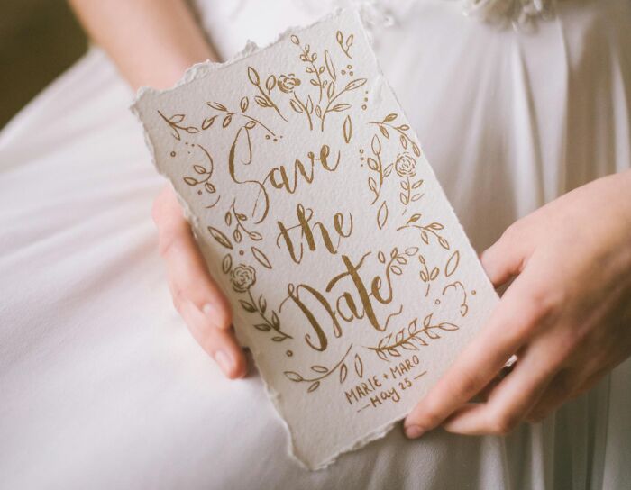 Persona sosteniendo una tarjeta de invitación decorativa en tonos dorados, símbolo de venganza contra ex parejas.