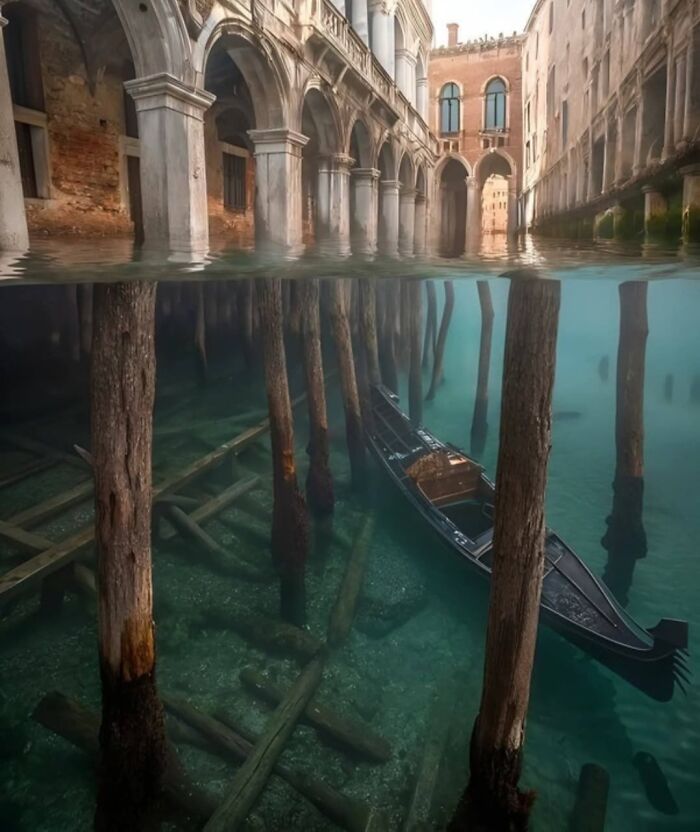 Canal de Venecia con góndola medio sumergida mostrando estructura de madera bajo el agua en escenario extraño y surrealista.