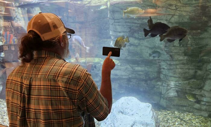 Hombre divertido en un acuario señalando peces, mostrando momentos en los que nunca dejó de comportarse como un niño.