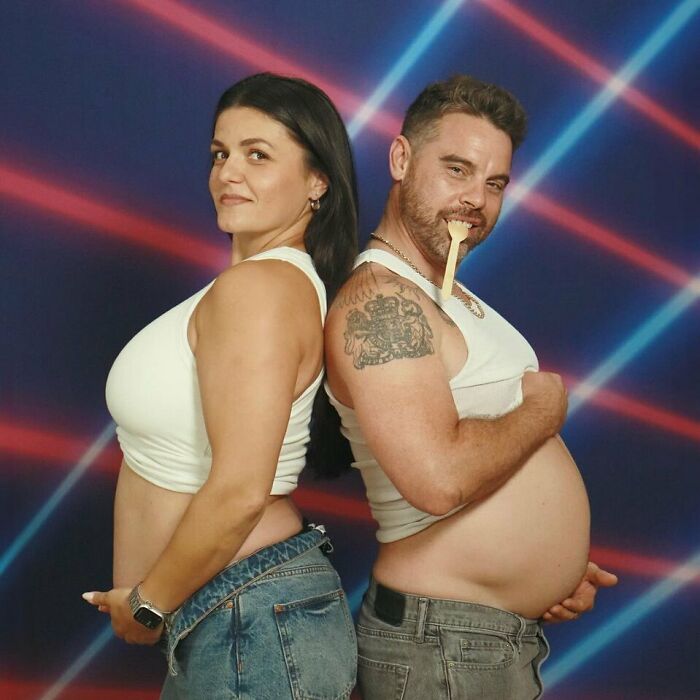 Pareja posando para foto familiar con divertidos errores, mostrando barriga falsa y sonrisas en fondo con luces de neón.