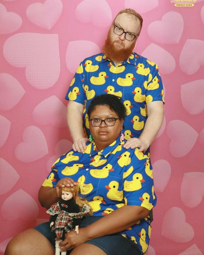 Pareja vestida con camisas de patitos, posando en fondo rosa con corazones, ejemplo divertido de fallas familiares.