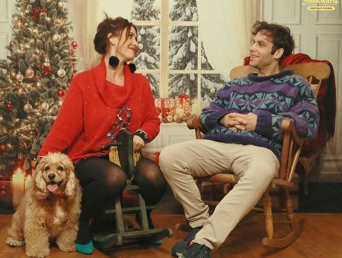 Pareja sonriente con su perro en suéteres navideños, posando para una foto familiar divertida y memorable.