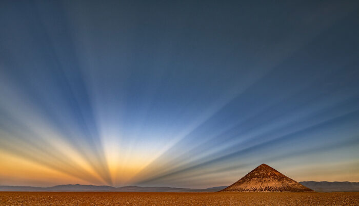 Montaña solitaria en un desierto extenso al amanecer con rayos de luz natural, imagen ganadora fotografía de naturaleza.