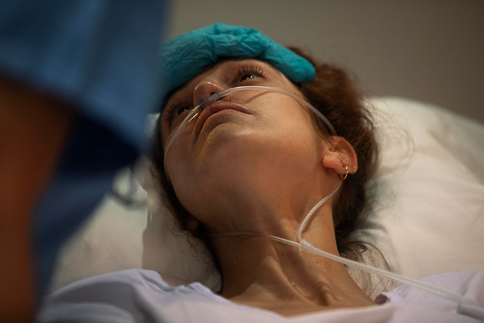 Paciente en cama hospitalaria con cánula nasal, mientras un médico en bata azul la atiende en un momento crítico de cirugía.