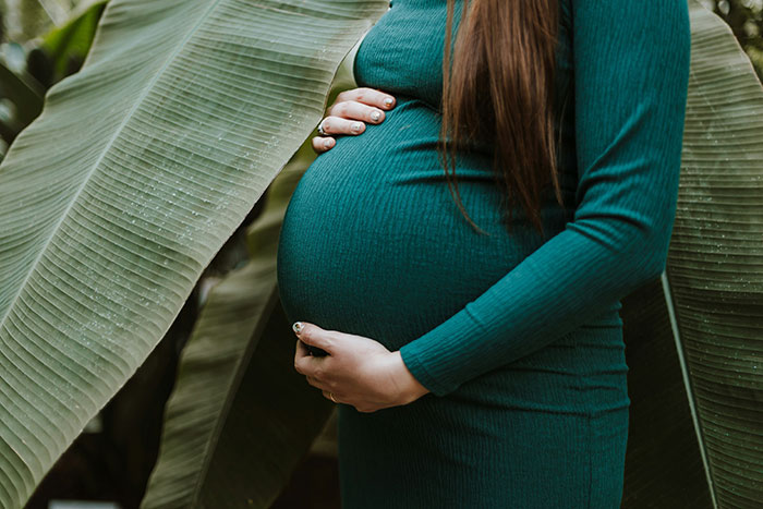 Mujer embarazada con vestido verde tocando su vientre en un entorno natural, relacionado con cirujanos y momentos críticos médicos.
