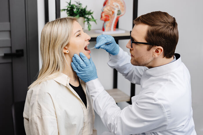 Paciente visibly embarrassed during a medical exam with doctor checking throat, capturing awkward trips to the doctor moment.