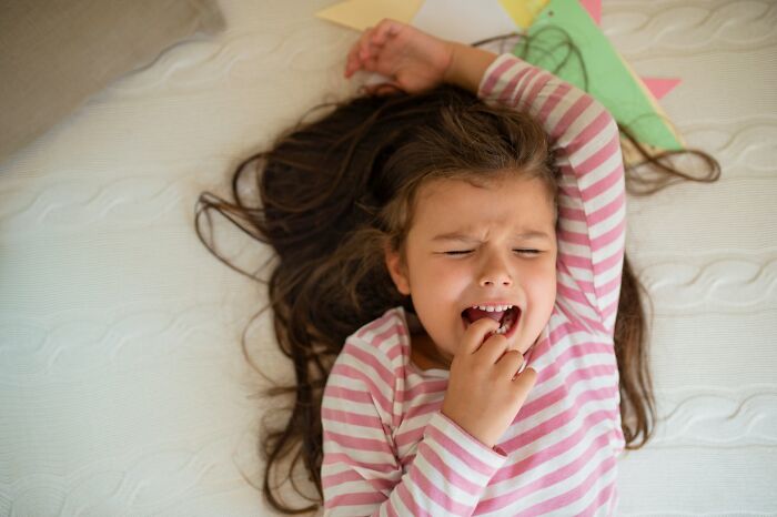 Niña con camiseta de rayas llorando en cama, representando momentos en que padres notan comportamiento difícil de sus hijos.