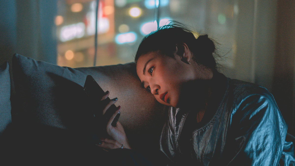 Mujer pensativa en un sofu00e1 oscuro mirando su telu00e9fono, su00edmbolo de posts que parecu00edan honestos hasta revelar su verdad.