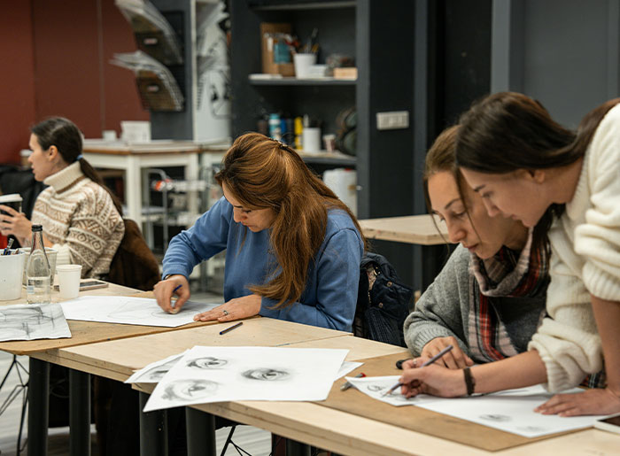 Personas en taller de arte dibujando rostros, mostrando concentración y comunicación social en un ambiente creativo.