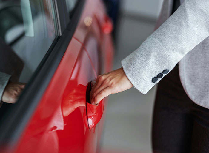 Mano de mujer abriendo la puerta de un coche rojo, simbolizando señales sociales mal interpretadas y situaciones incómodas.