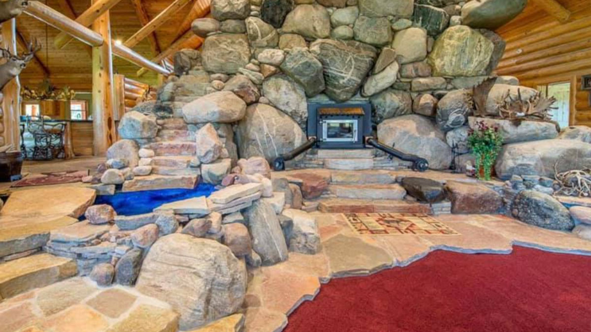Interior con chimenea rodeada de grandes piedras y piscina pequeu00f1a en listado de Zillow que parece falso.
