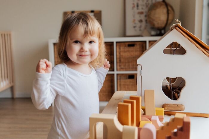 Niña pequeña sonriendo en casa jugando con juguetes de madera, reflejando momentos de padres con hijos difíciles.