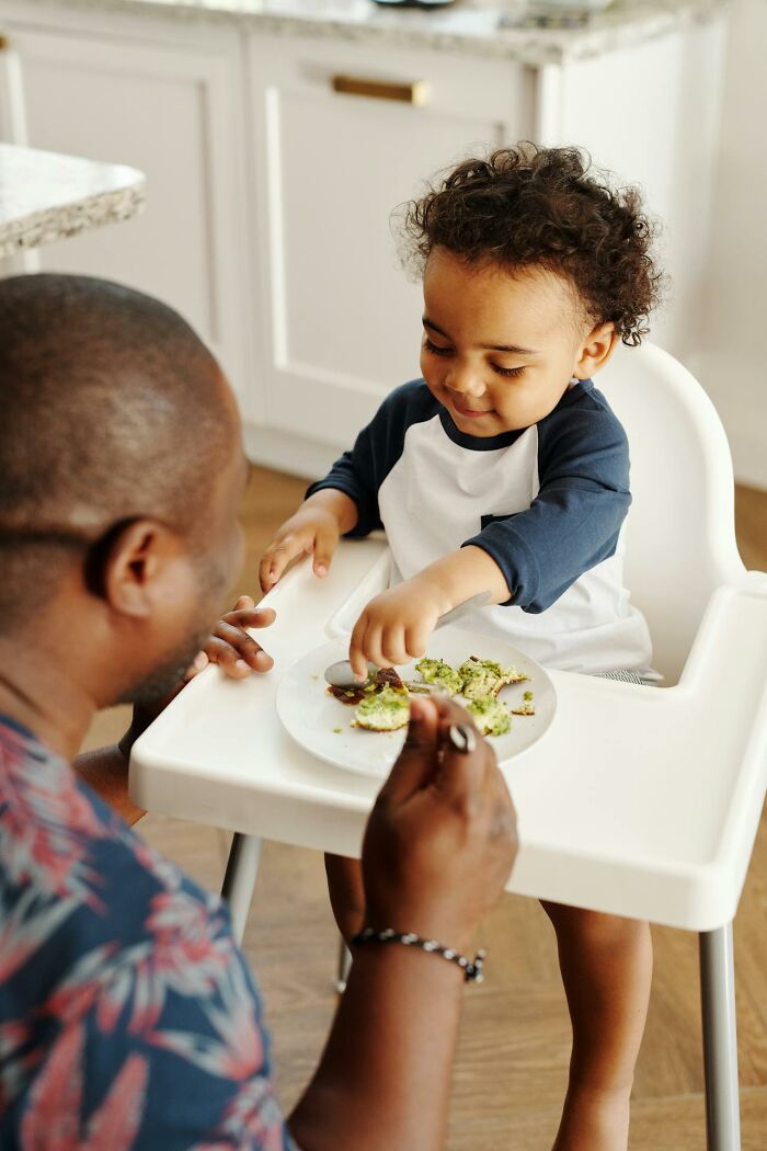 Padre alimentando a su hijo pequeño en una silla alta, momentos que revelan el verdadero carácter de los niños según padres.