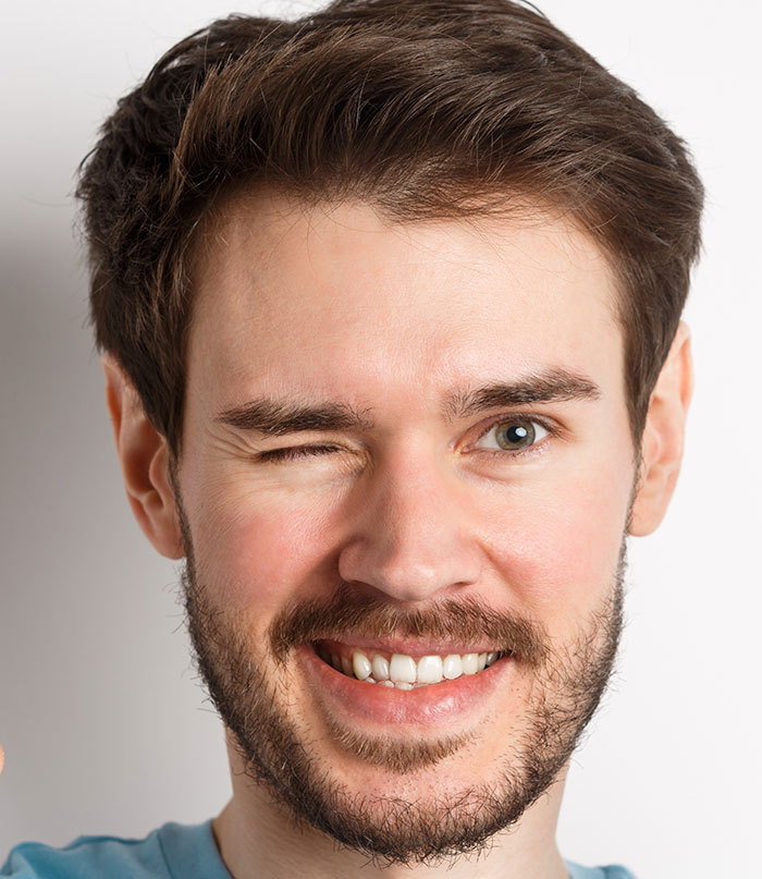 Hombre joven guiñando un ojo y sonriendo, mostrando sorpresa y nerviosismo tras vivir las mentiras contadas.