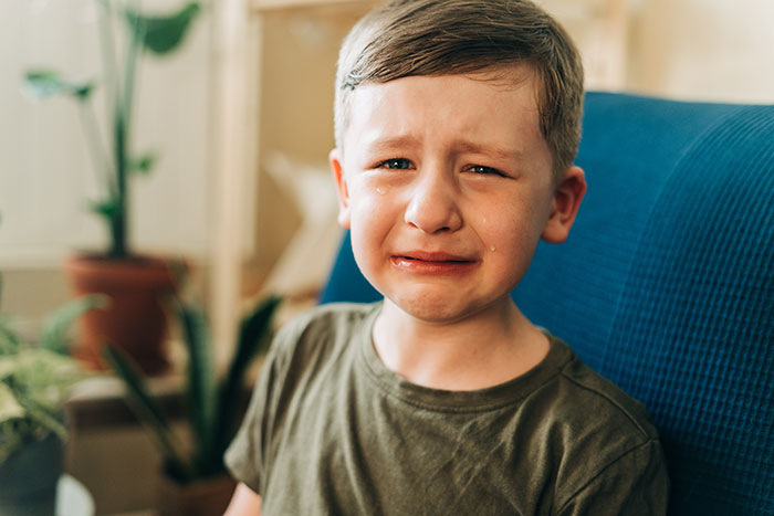Niño llorando con lágrimas en el rostro, mostrando tristeza y choque emocional en un ambiente hogareño desenfocado.
