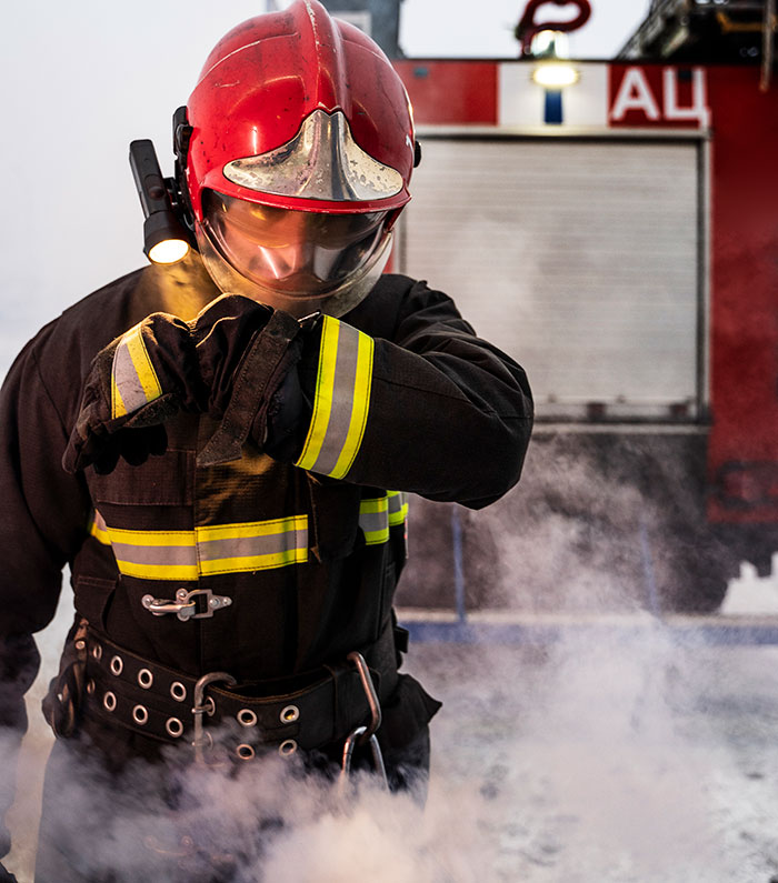Bombero con casco rojo y equipo reflectante cubriéndose del humo en escena de emergencia, shockeado por la situación actual.