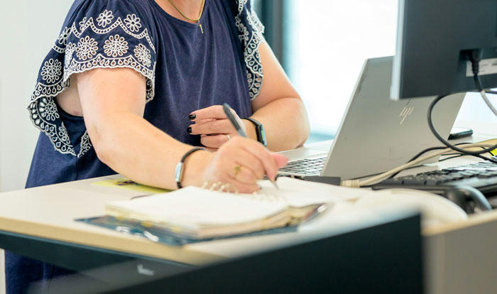 Persona escribiendo en una libreta frente a computadora en oficina, ilustrando escándalos laborales que impactaron el ambiente laboral.
